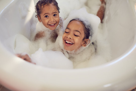 Portrait playful sisters enjoying bubble bath