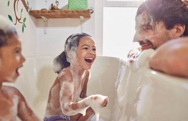 Playful daughters in bathtub wiping bubbles on father‚Äôs face