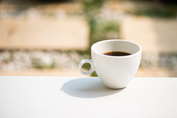 A white cup and black coffee on nature ground