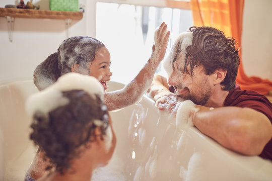 Playful daughters in bubble bath wiping bubbles on father&sbquo;&Auml;&ocirc;s face