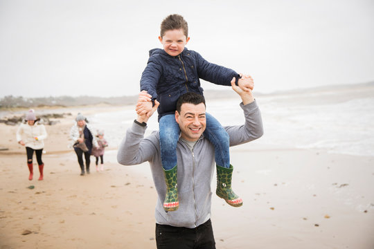Portrait playful father carrying son on shoulders on winter beach