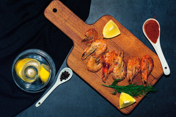 fresh shrimps served on a wood blackboard with lemon, black peppercorns and chili in spoon. Dark...