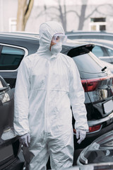 asian epidemiologist in hazmat suit and respirator mask inspecting cars on parking lot
