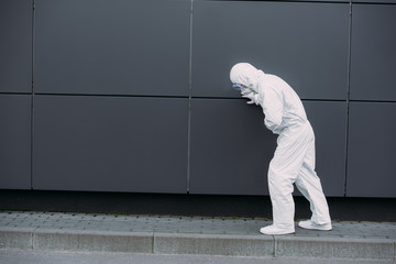 Fototapeta na wymiar asian epidemiologist in hazmat suit leaning on wall while suffering from symptomatic abdominal pain