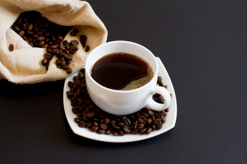 coffee beans in a bag with a white Cup of fresh coffee on a black background. space for text, top view.