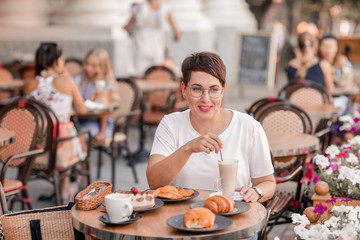 Woman stirs milkshake at table. European woman with short hair in Paris drinks hot drinks and eats...
