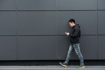 side view of young asian man chatting on smartphone while walking along wall