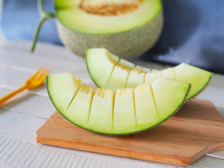 Pieces of green net melon fruit or honeydew on wooden chopping board for healthy eating or dietary food concept.