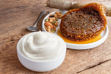 Healthy flavored yogurt in ceramic bowl with granola and honey comb on the wood background. Food and healthy concept.