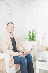 Handsome man working with laptop at home sitting on couch