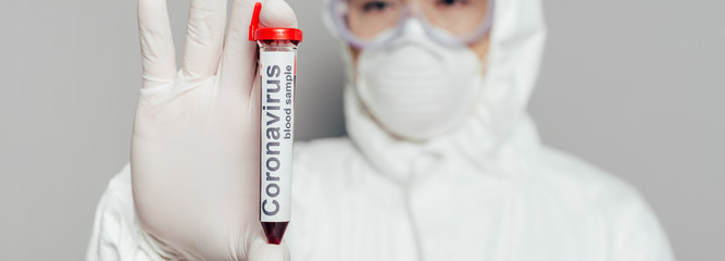 selective focus of asian epidemiologist in hazmat suit and respirator mask showing test tube with...