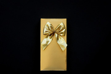 golden box with a golden bow on a black background. Concept of gift and pleasant surprise