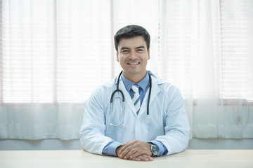 Young doctor caucasian man sitting at the desk at his working place and smiling looking at camera. Perfect medical service in clinic. Happy future of medicine and healthcare.