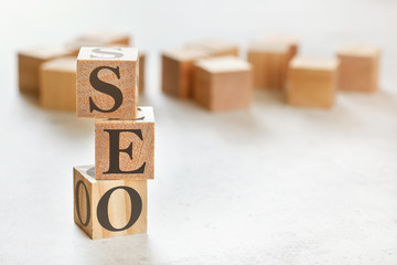 Three wooden cubes with letters SEO (means Search Engine Optimization), on white table, more in background, space for text in right down corner