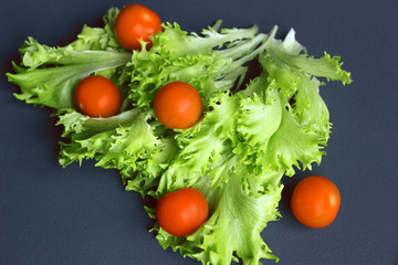 Cherry tomatoes and lettuce lie on a dark surface. Ripe cherry tomatoes. Tomatoes are on the table. Tomato sliced. Halved cherry tomatoes.