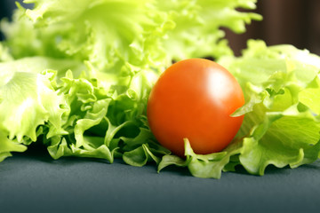 Cherry tomatoes and lettuce lie on a dark surface. Ripe cherry tomatoes. Tomatoes are on the table. Tomato sliced. Halved cherry tomatoes.