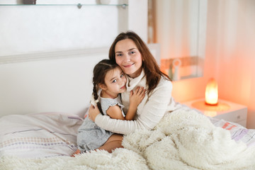Tender Caucasian mom and daughter hugging on bed