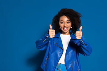 smiling african american woman showing thumbs up on blue background