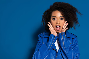 shocked african american woman with hands near face on blue background