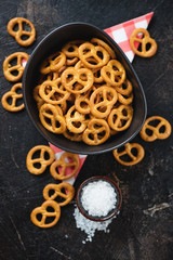Bowl of pretzels with sea salt over dark brown stone surface, flatlay, view from above