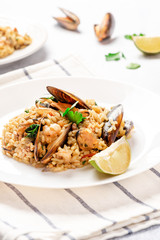 Seafood risotto in a white plate on the served table. Risotto with shrimp, tomatoes, parsley and mussels in shells. Tasty and healthy Mediterranean cuisine.