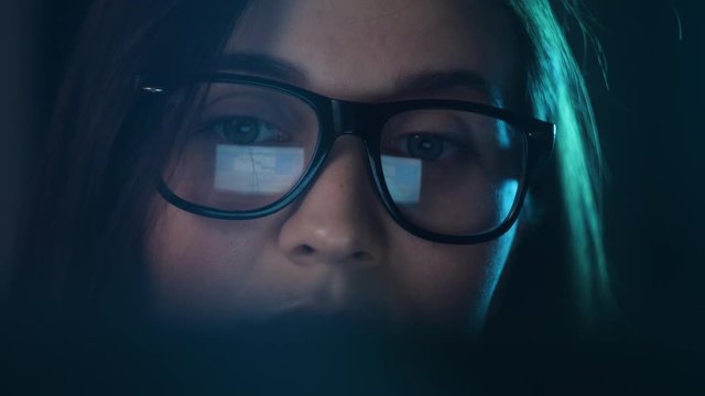 Close up of tired woman working at night on laptop, girl in eye glasses with reflections overworking busy, using computer in dark office