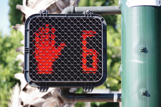 Pedestrian crosswalk traffic signal at a city intersection with a red hand warning to not enter because only six seconds left for crossing