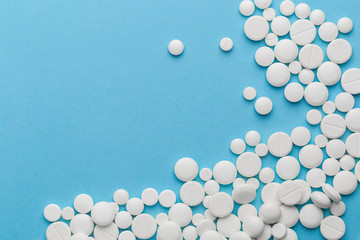 scattered white pills on a blue table. Layout for special offers such as advertising or other ideas. The concept of medicine, pharmacy and healthcare. Space for copy. flat lay for text or logo.