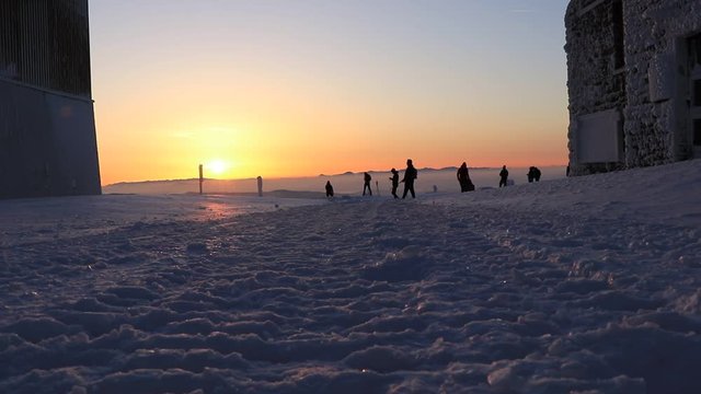 On the horizon, people are walking back and forth at sunrise between buildings. Tourists looks like ghosts. Peak of mountain full of humans at sunrise. Beskydy, Lysa Hora, czech republic in Europe.