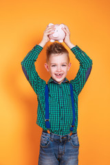Cute little boy shaking piggy box on orange background