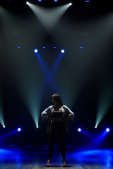 Obraz premium Girl in black suit performing on stage with bright blue background