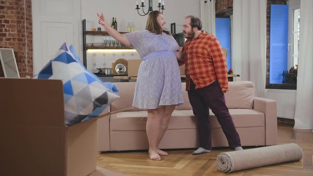 Funny fat man and woman dancing with joy in new apartment
