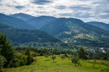 Fototapeta na wymiar Beautiful panorama of the Carpathian village against backdrop of scenic mountains, where the highlanders live Hutsul. Wild forests, fields pastures, Ukraine 