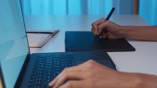Cheerful young graphic designer lady using digital graphic tablet while working late in modern office at night, Asia professional female using laptop computer retoucher sitting in living room at home.