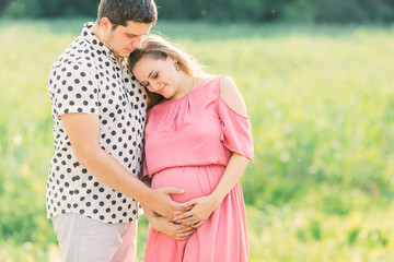 young woman leaning against her husband and they touch the tummy