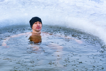 The guy in the hat relaxed closing his eyes, swimming in the winter in the icy water of the lake