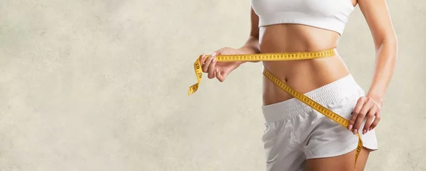 Poster Beautiful fitness girl measuring her waistline with measure tape © BillionPhotos.com