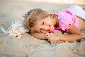 portrait of a little blonde girl lying on a sandy beach. lifestyle, space for text