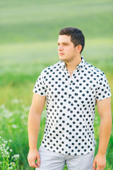 stylish guy in polka dot shirt on field among grass looks to the