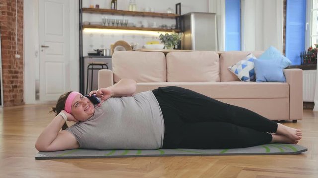 Overweight woman lying on mat on floor and talking on phone