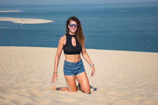 Portrait belle et charmante jeune femme caucasian brune aux yeux bleu joyeuse et confiance en soi s&eacute;duisante chanceuse charismatique fran&ccedil;aise europ&eacute;enne heureuse zen &agrave; genoux dune du pilat oc&eacute;an