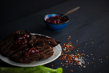 fresh grilled steaks, wild meat with spices on a black background, the concept of food with no GMOs