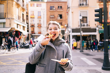 A happy blonde Caucasian girl eats pizza on a city street