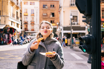 A happy blonde Caucasian girl eats pizza on a city street