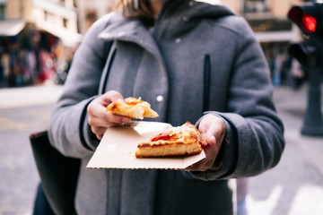 A happy blonde Caucasian girl eats pizza on a city street