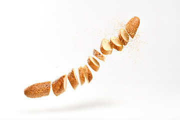 Baguette mit Sesamsamen, der in der Luft fliegt. Frisch gebackenes Brot in Scheiben geschnitten, geschnitten. Französisches Baguette der traditionellen Backwaren. Köstliches knuspriges Weizenbrot, Levitation, Fly-Food-Konzept