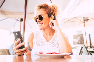 Beautiful and happy adult model woman use modern cellular phone at the restaurant with wifi connection - cheerful people and technology - modern lady with sunglasses