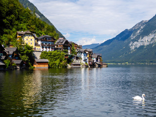 Fototapeta na wymiar Idyllic small village located by the lake in Hallstatt, Austria. There is a tall church tower in the middle of the village. Alpine village. High mountains rising from the lake. Swam crossing the lake