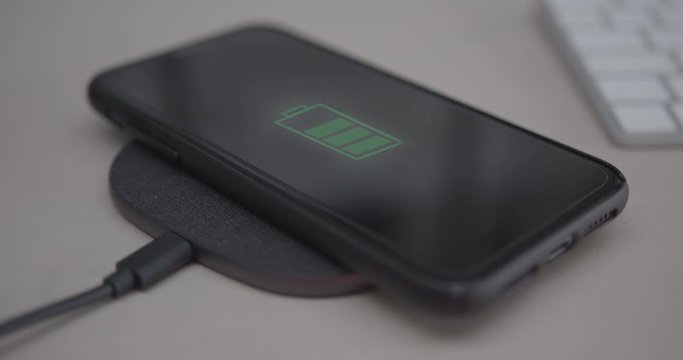 Close up of Smart Phone battery being charged on wireless charger on desk