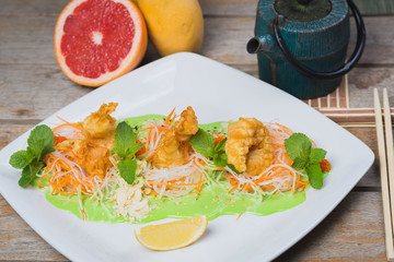 Shrimp in batter with vegetables and herbs on a plate on a wooden table in a restaurant.